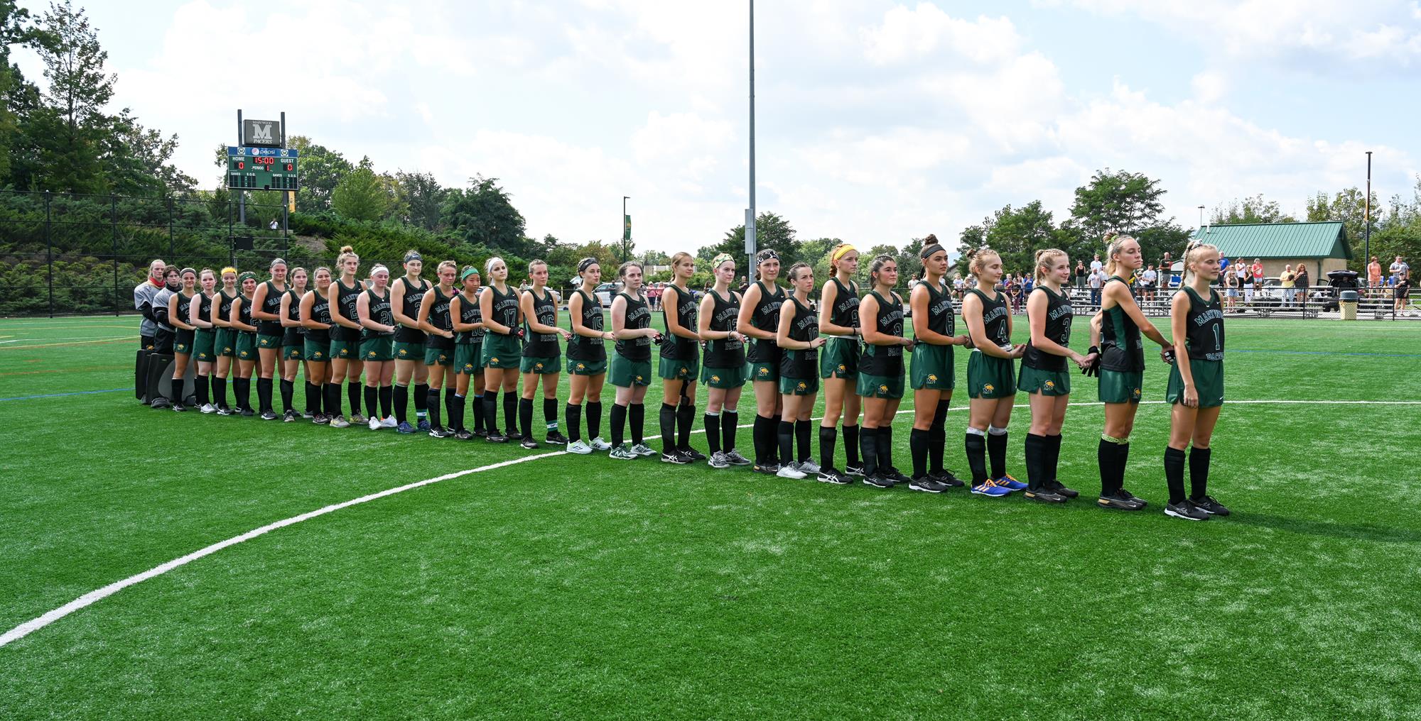Marywood field hockey lines up before a game in black and green uniforms.