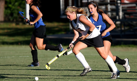 Field hockey player dribbling the ball in a white and black uniform.