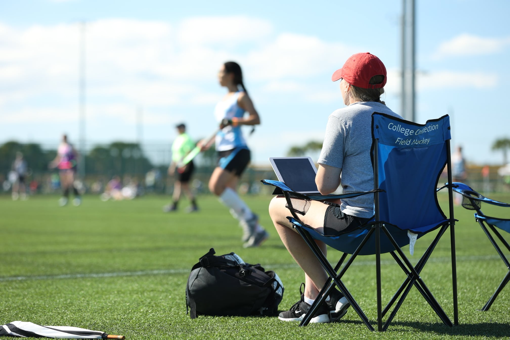 Coach sits on the sideline of a field hockey game.