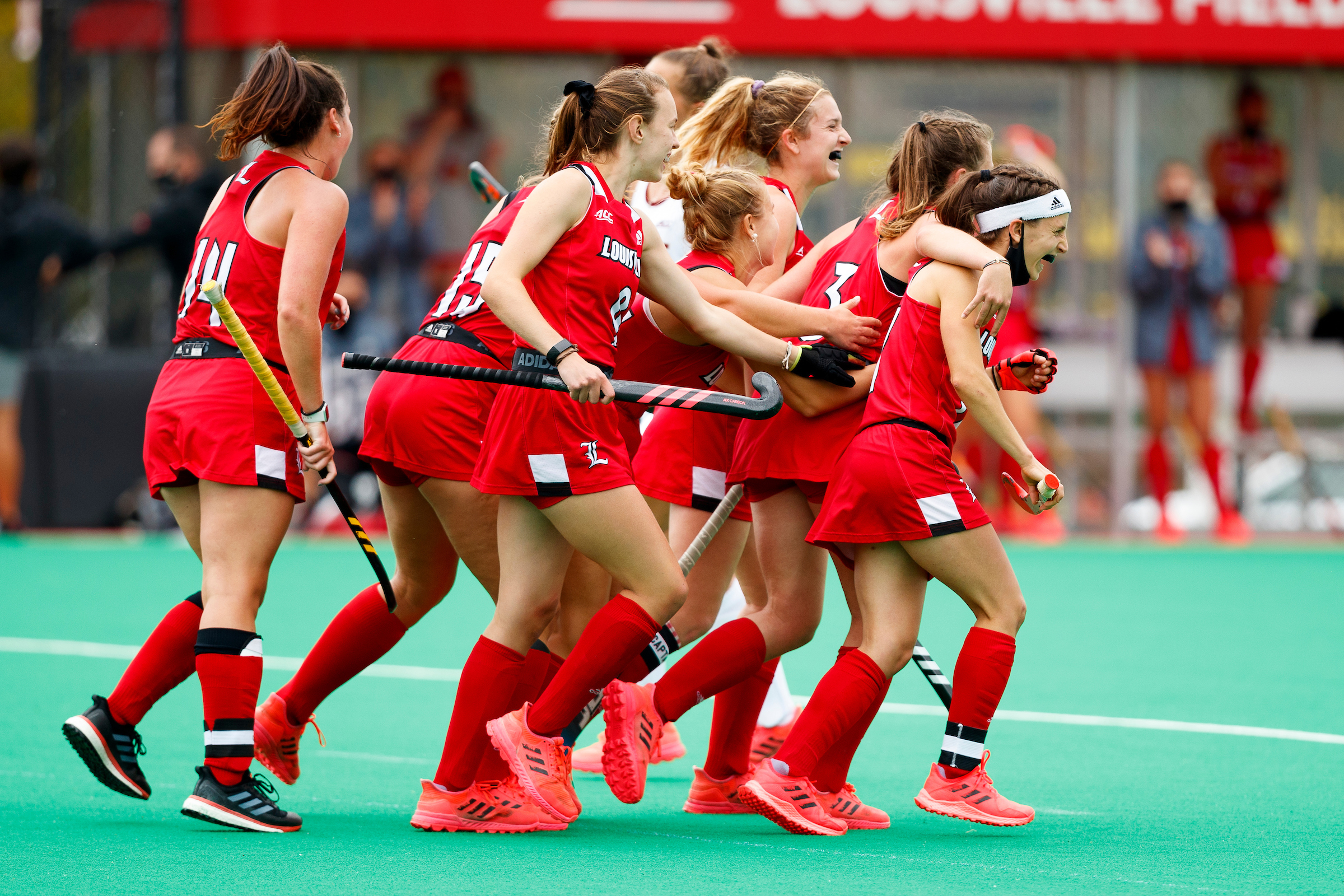 The University of Louisville team celebrates after a goal with a group hug in red uniforms.