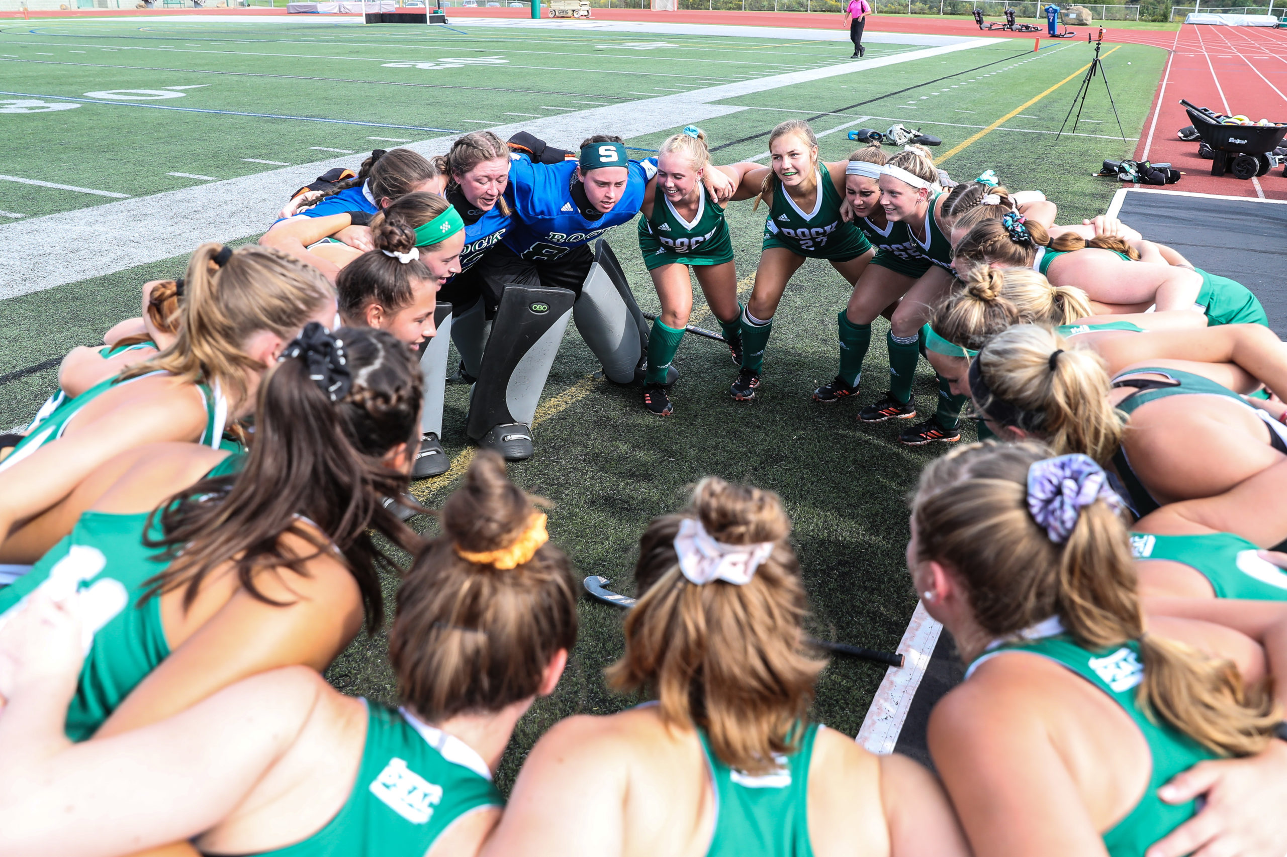 The Slippery Rock University field hockey team huddles in a circle in green uniforms.